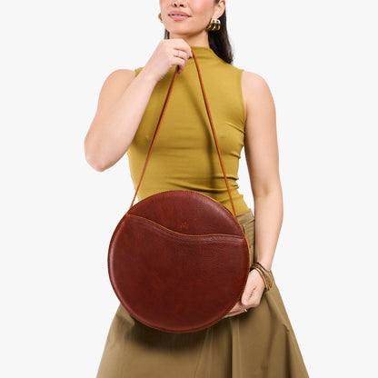 Nutmeg | Model carrying large circle shaped leather bag with top zipper and carrying strap