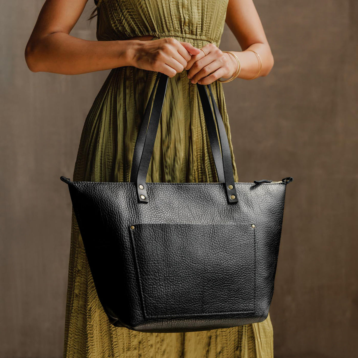 Pebbled--black*Zipper | Model holding large zipper leather tote bag with sturdy bridle handles and front pocket