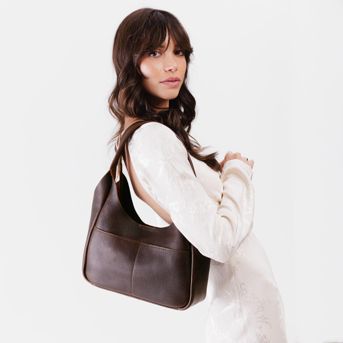 Coldbrew*Medium | A model holding a u-shaped, flat-bottomed leather shoulder bag with two outside pockets