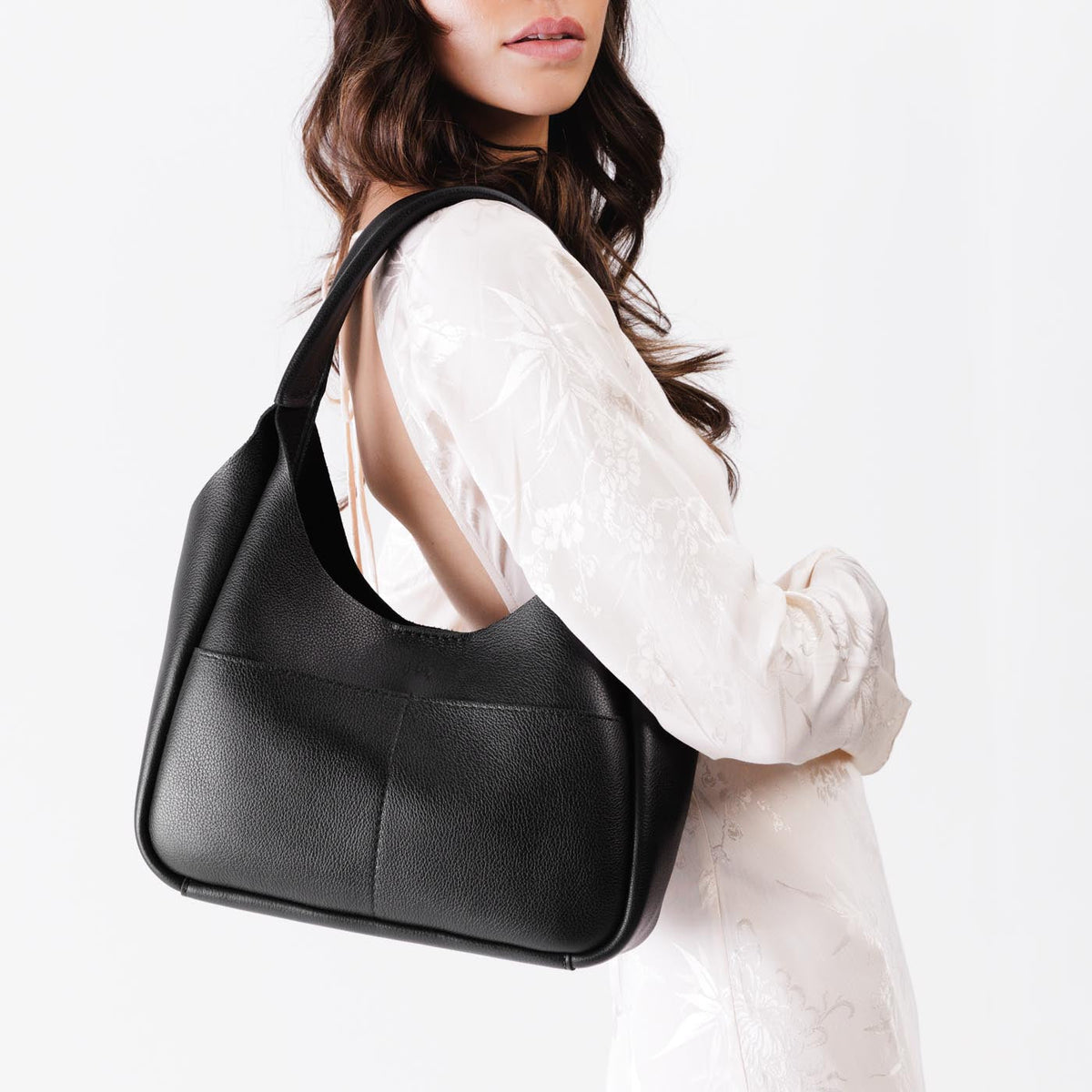 Pebbled--Black*Medium | A model holding a u-shaped, flat-bottomed leather shoulder bag with two outside pockets